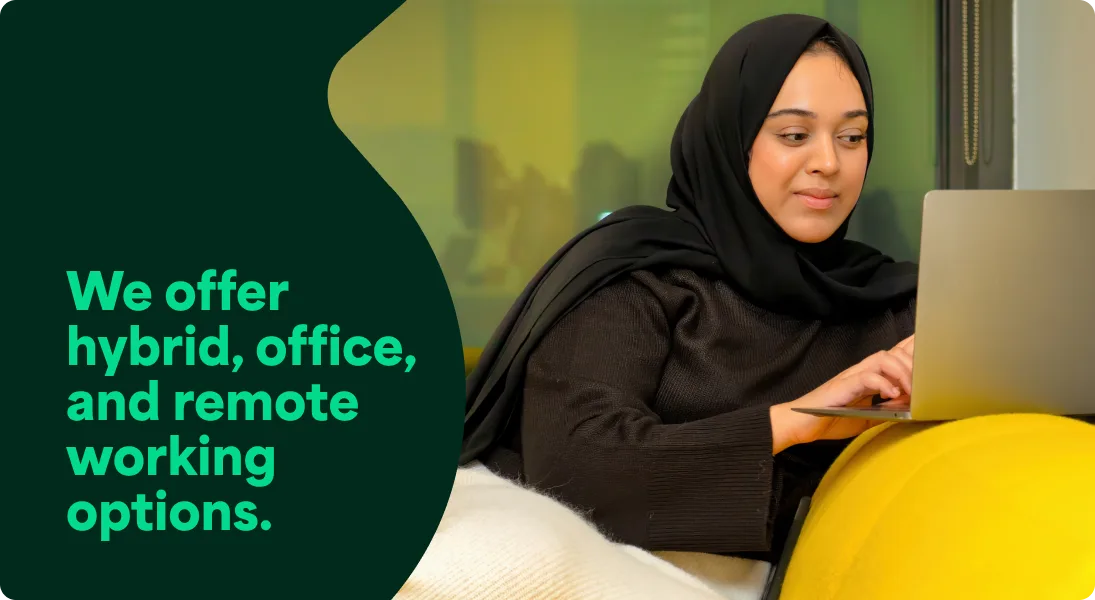 A photo of a Trustpilot employee working on her laptop on the couch in the office. It has a text overlay that says We offer hybrid, office, and remote working options.